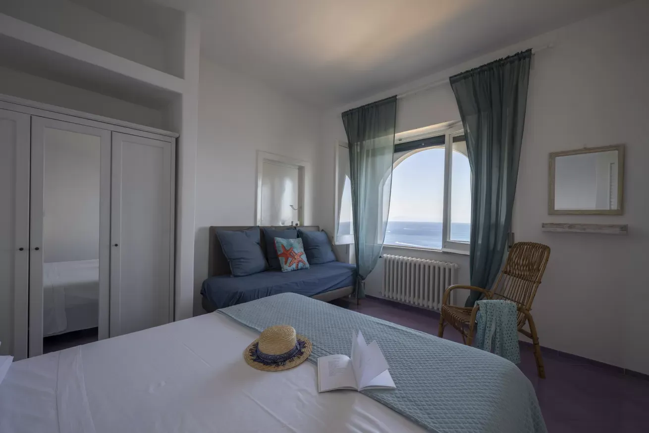 Camera da letto con divano, letto matrimoniale e ampia finestra affacciata sul mare