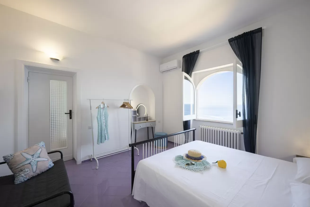 Camera da letto luminosa con vista sul mare, letto matrimoniale, divano, toeletta e finestra ad arco aperta