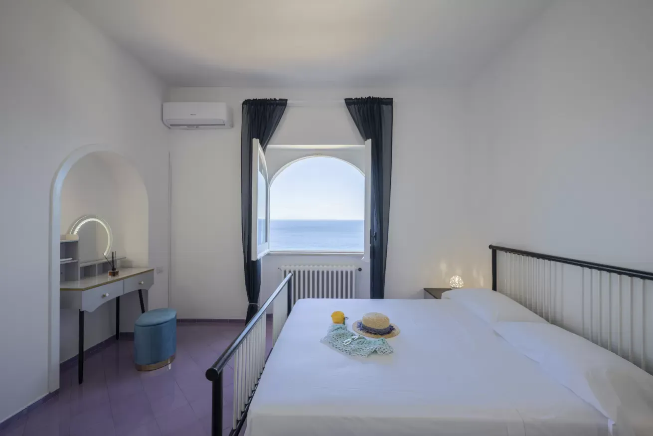 Camera da letto con letto matrimoniale, finestra ad arco affacciata sul mare e toeletta