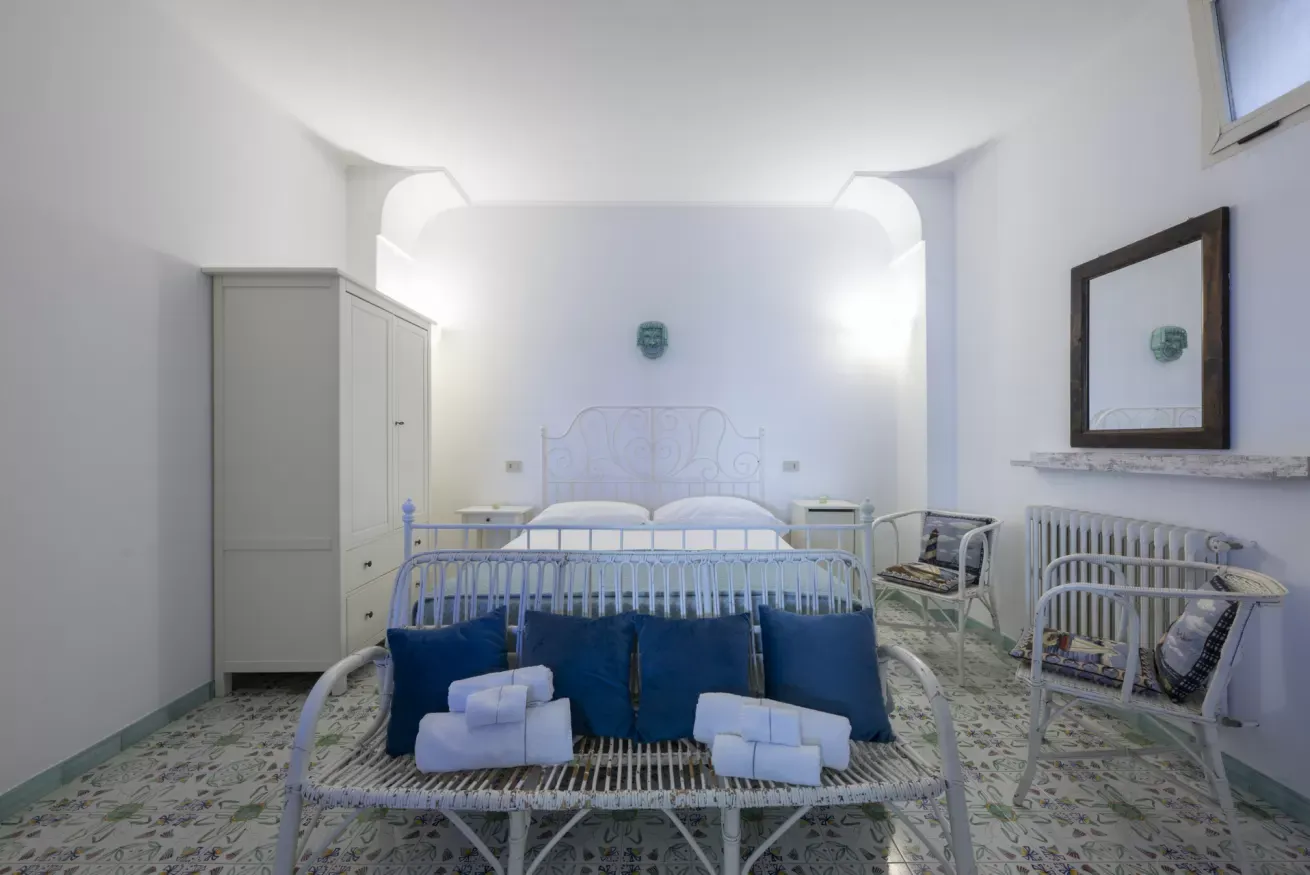 Camera da letto luminosa con letto matrimoniale, divanetto ai piedi, armadio, poltrone e pavimento decorato