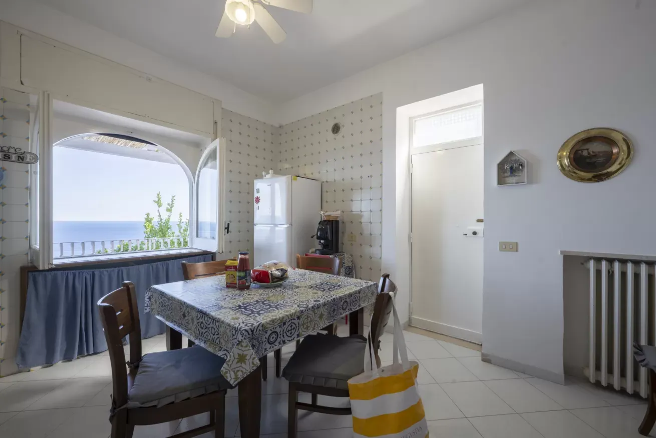 Cucina abitabile con tavolo apparecchiato, frigorifero e vista sul mare dalla finestra