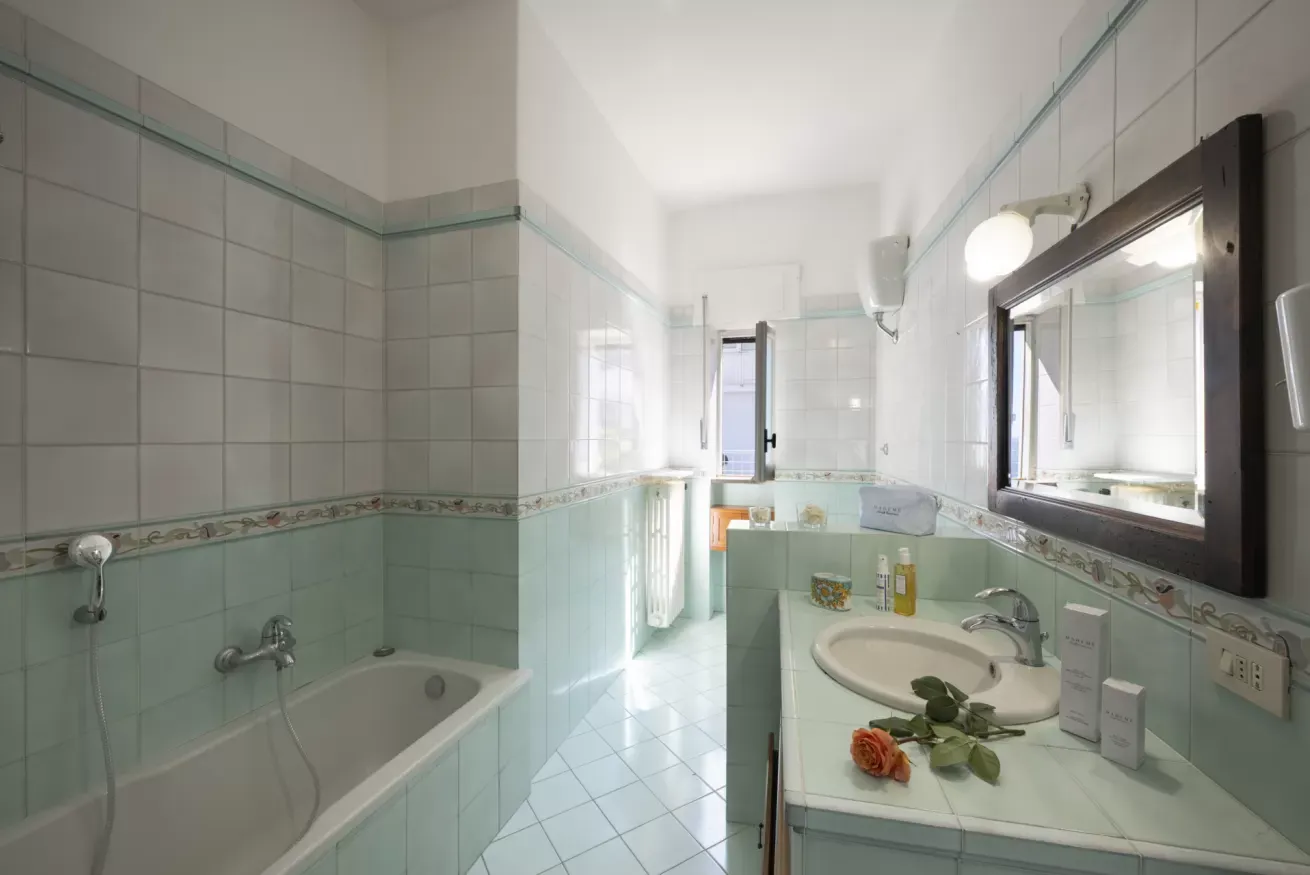 Bagno luminoso con vasca, lavabo, specchio e piastrelle bianche e verde chiaro