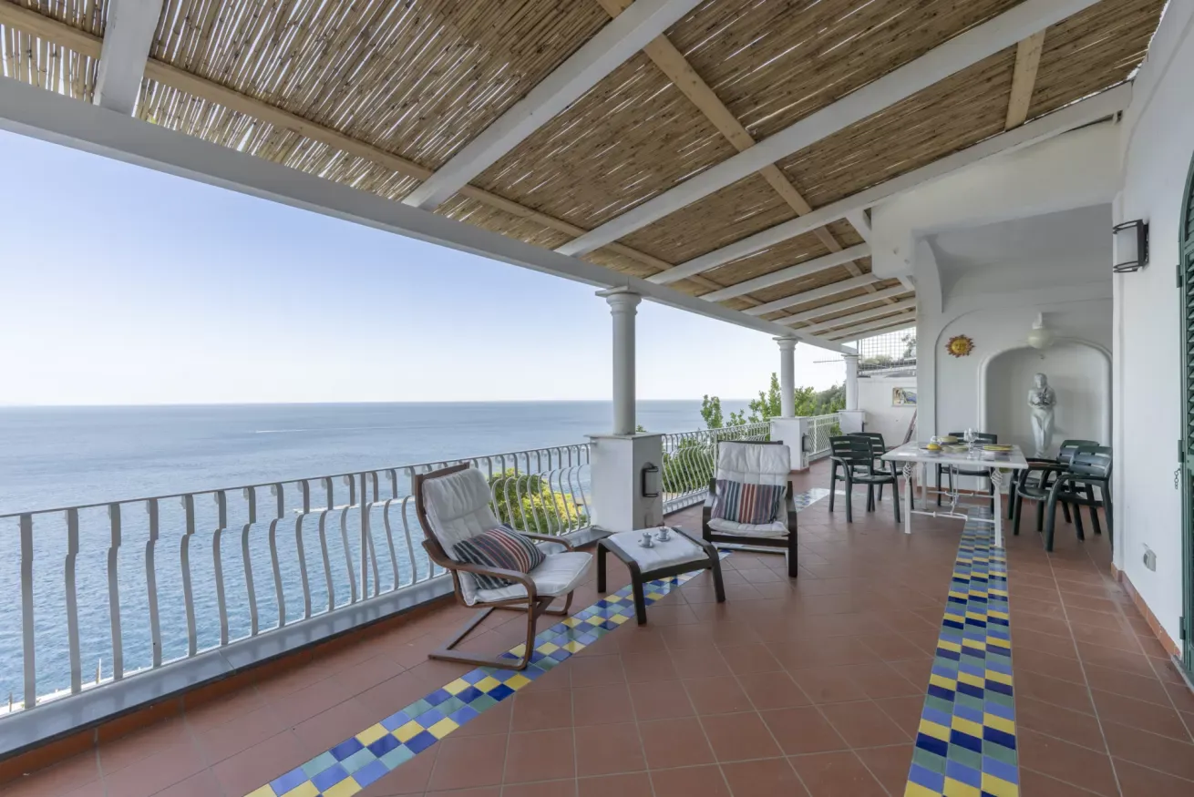Terrazza panoramica sul mare con pergolato, sedie a sdraio, tavolo da pranzo e piastrelle decorative colorate